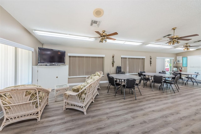 dining room featuring ceiling fan, vaulted ceiling, light hardwood / wood-style flooring, and a textured ceiling