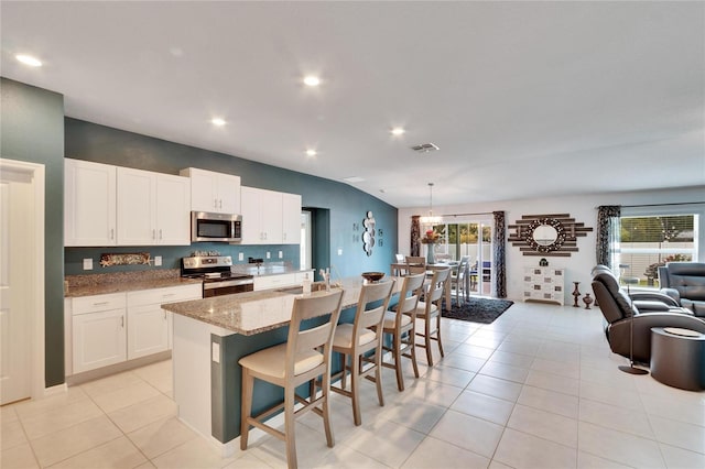 kitchen with a breakfast bar area, white cabinetry, an island with sink, stainless steel appliances, and light stone countertops