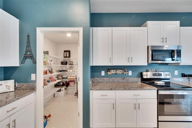 kitchen featuring stainless steel appliances, light tile patterned floors, white cabinets, and light stone counters