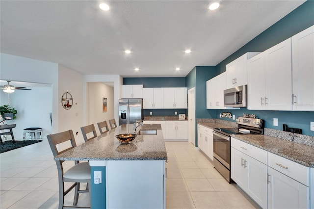 kitchen featuring stainless steel appliances, an island with sink, white cabinets, and a kitchen bar