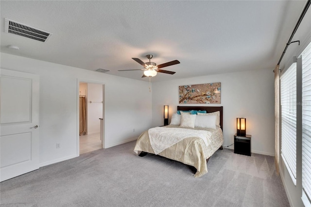 bedroom featuring ceiling fan, connected bathroom, light carpet, and a textured ceiling