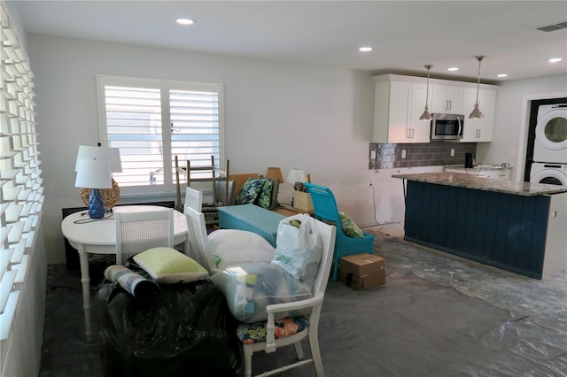 kitchen featuring white cabinetry, pendant lighting, stacked washer / dryer, light stone countertops, and backsplash