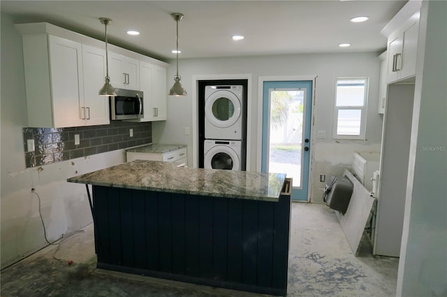 kitchen featuring decorative light fixtures, white cabinets, decorative backsplash, stacked washer and clothes dryer, and light stone countertops