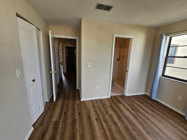 unfurnished bedroom featuring dark hardwood / wood-style flooring, a closet, a textured ceiling, and ensuite bathroom