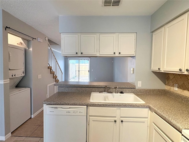 kitchen featuring sink, white dishwasher, stacked washer / drying machine, white cabinets, and decorative backsplash