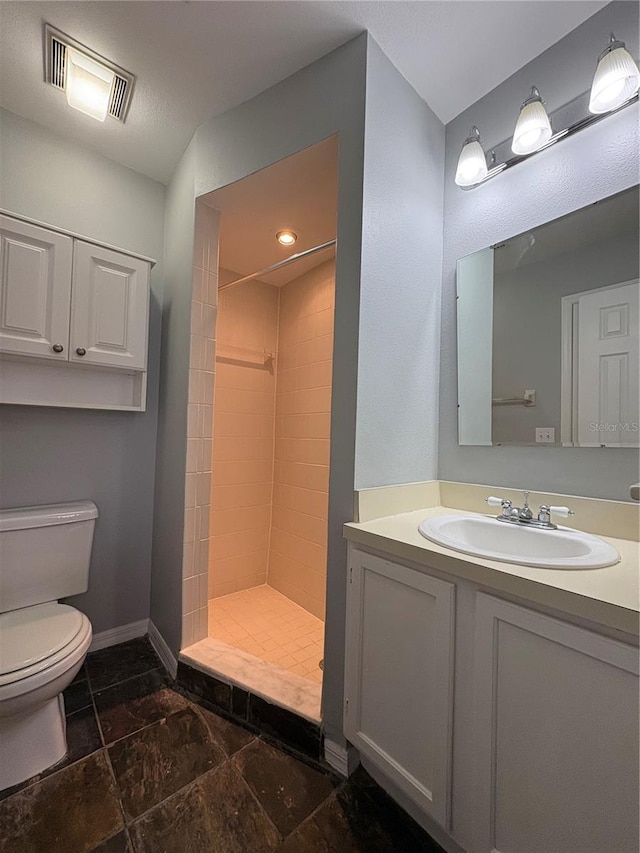 bathroom featuring vanity, tiled shower, and toilet