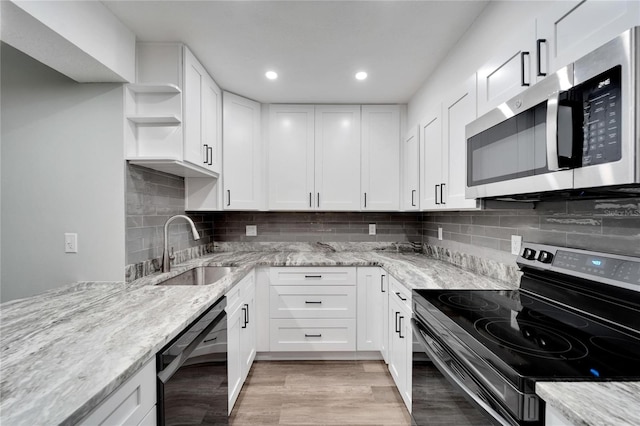 kitchen with sink, white cabinetry, light wood-type flooring, appliances with stainless steel finishes, and light stone countertops