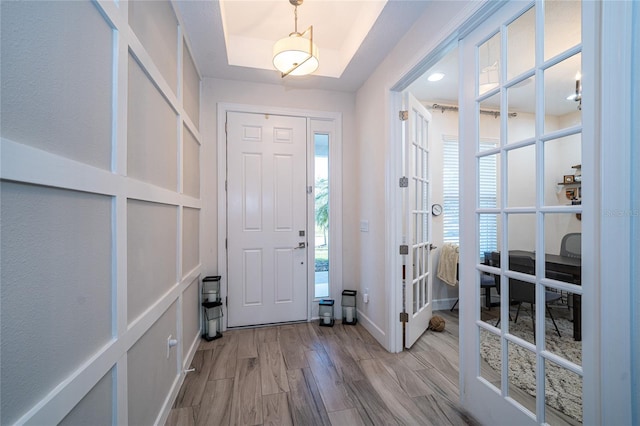 entrance foyer with french doors, a tray ceiling, and light hardwood / wood-style floors