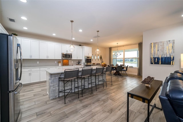 kitchen with pendant lighting, appliances with stainless steel finishes, a kitchen breakfast bar, white cabinets, and a center island with sink