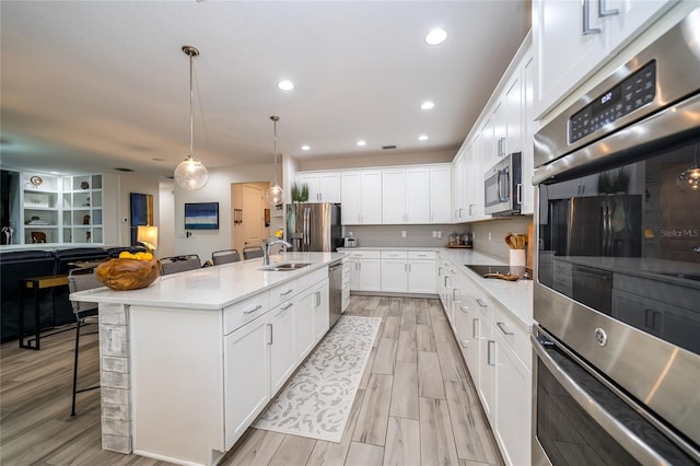 kitchen featuring sink, a breakfast bar area, appliances with stainless steel finishes, hanging light fixtures, and a center island with sink