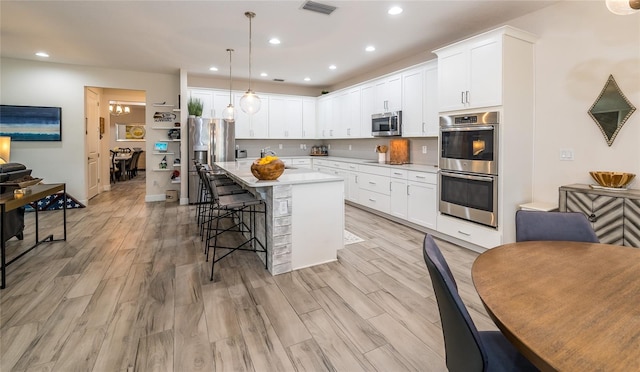 kitchen featuring stainless steel appliances, hanging light fixtures, a center island, and white cabinets