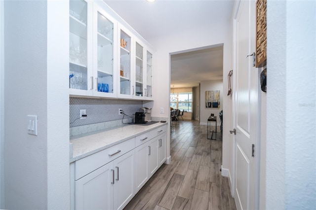 bar with white cabinetry, light stone countertops, light hardwood / wood-style floors, and decorative backsplash