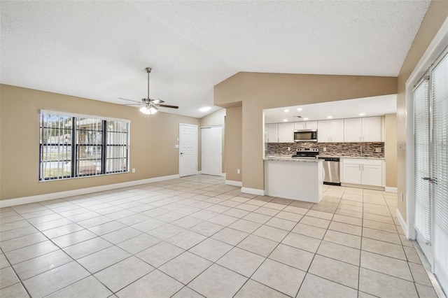 kitchen featuring lofted ceiling, light stone counters, stainless steel appliances, and white cabinets