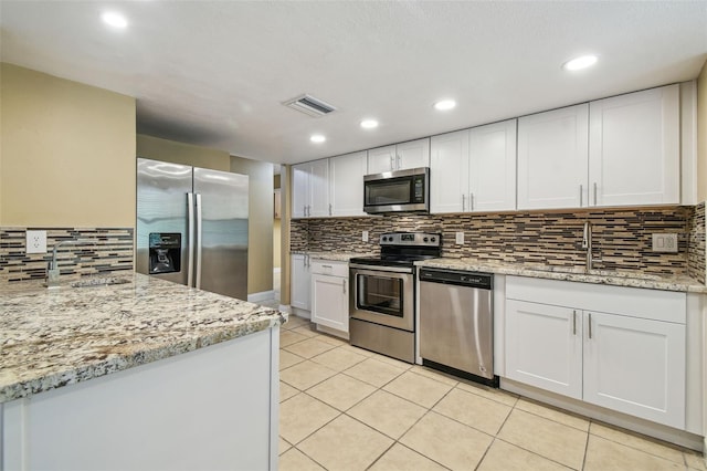 kitchen featuring appliances with stainless steel finishes, tasteful backsplash, white cabinets, light tile patterned floors, and light stone counters