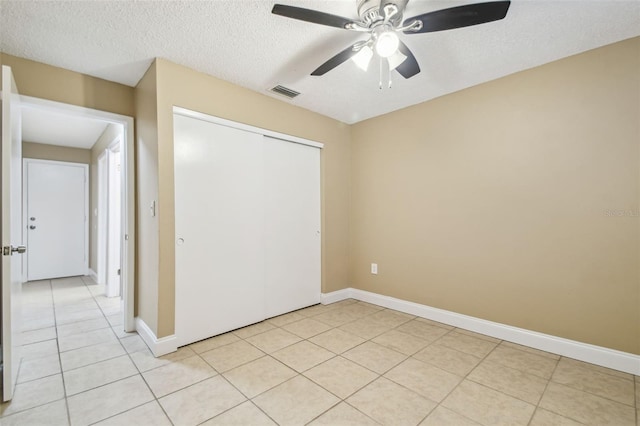 unfurnished bedroom featuring light tile patterned flooring, a textured ceiling, ceiling fan, and a closet