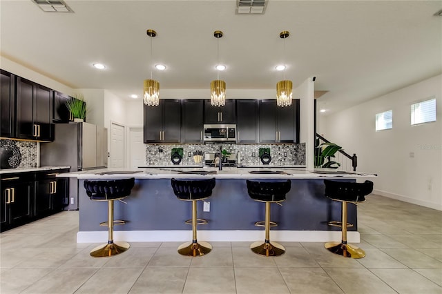 kitchen featuring appliances with stainless steel finishes, a kitchen breakfast bar, hanging light fixtures, and a center island with sink