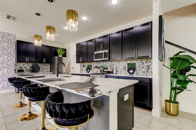 kitchen featuring decorative light fixtures, light tile patterned floors, appliances with stainless steel finishes, a kitchen breakfast bar, and a kitchen island with sink