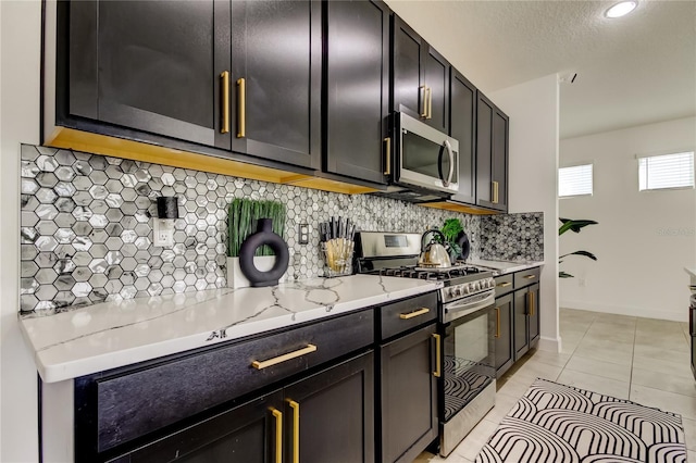 kitchen featuring appliances with stainless steel finishes, backsplash, light tile patterned floors, light stone counters, and a textured ceiling