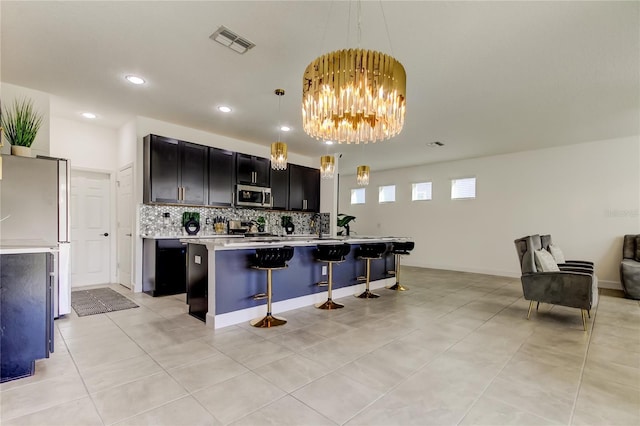 kitchen with a breakfast bar area, a kitchen island with sink, hanging light fixtures, fridge, and a chandelier