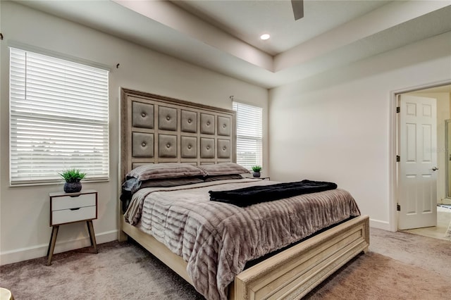 carpeted bedroom with a raised ceiling and ceiling fan