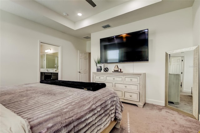 carpeted bedroom with ensuite bathroom, ceiling fan, and a tray ceiling