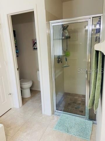 bathroom featuring tile patterned flooring, a shower with door, and toilet