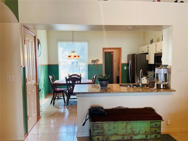 kitchen with light tile patterned floors, white cabinetry, a sink, dark stone counters, and a peninsula