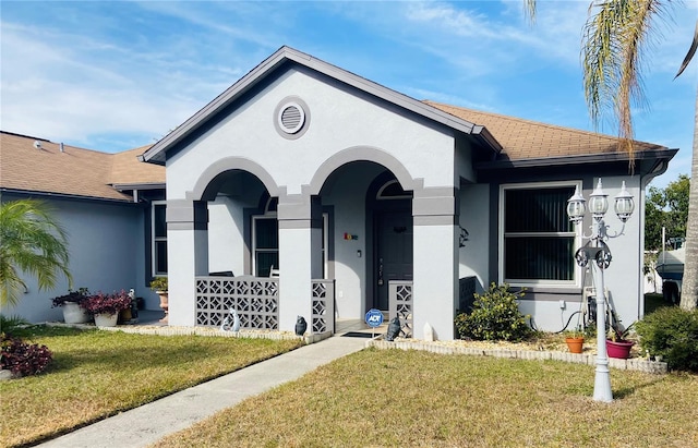 view of front facade featuring roof with shingles, a front yard, and stucco siding