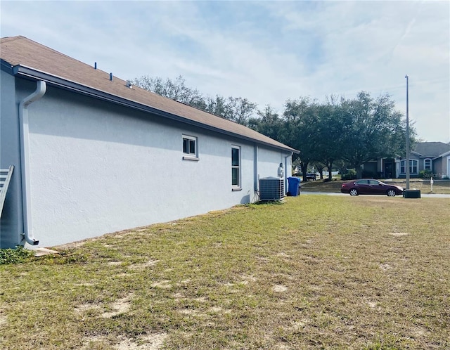 view of side of property featuring a yard, central AC unit, and stucco siding