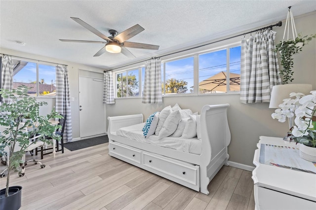 bedroom featuring ceiling fan, light hardwood / wood-style floors, multiple windows, and a textured ceiling