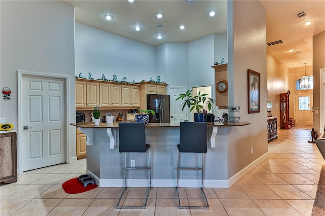 kitchen with black refrigerator, a kitchen bar, a high ceiling, light tile patterned flooring, and kitchen peninsula