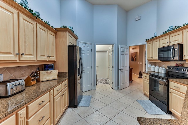 kitchen featuring tasteful backsplash, light tile patterned floors, a towering ceiling, dark stone counters, and black appliances