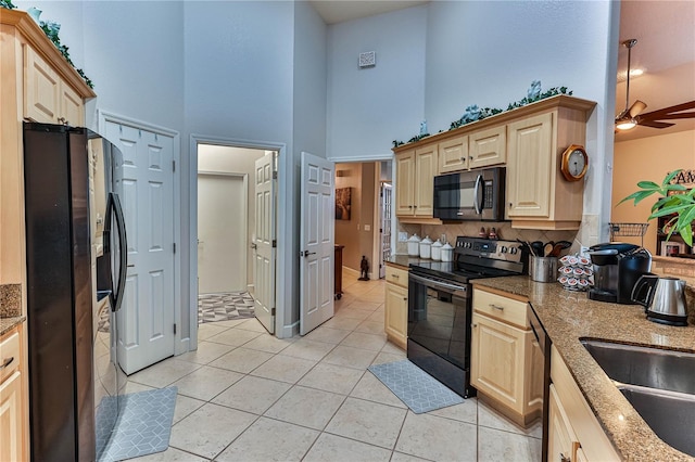 kitchen with light brown cabinetry, a high ceiling, light tile patterned floors, light stone counters, and black appliances