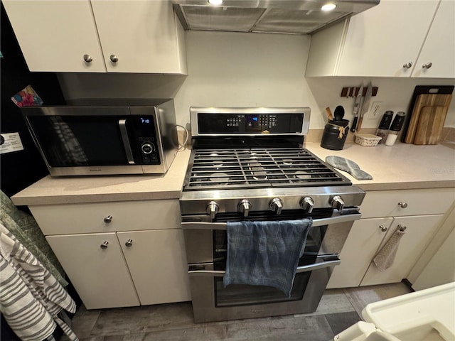 kitchen with dark wood-type flooring, range hood, white cabinets, and appliances with stainless steel finishes