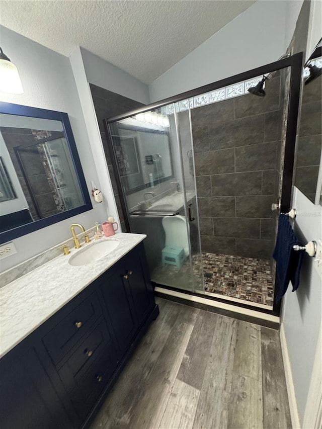 bathroom with hardwood / wood-style floors, a shower with shower door, lofted ceiling, vanity, and a textured ceiling