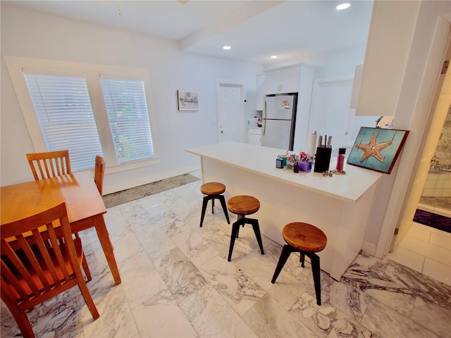 kitchen with white cabinetry, a breakfast bar, kitchen peninsula, and white fridge