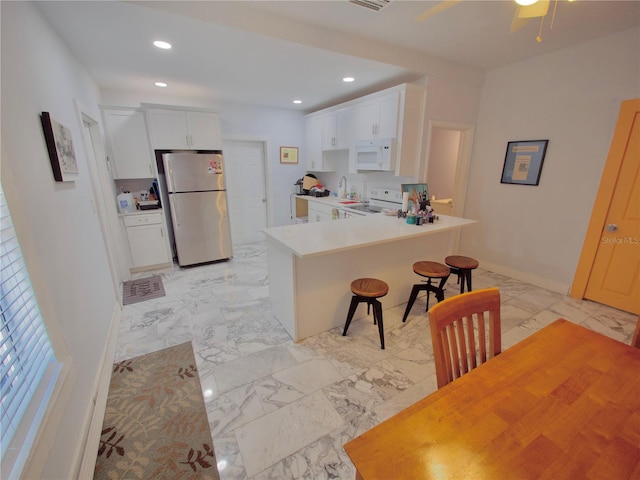 kitchen featuring white appliances, a breakfast bar area, ceiling fan, white cabinets, and kitchen peninsula