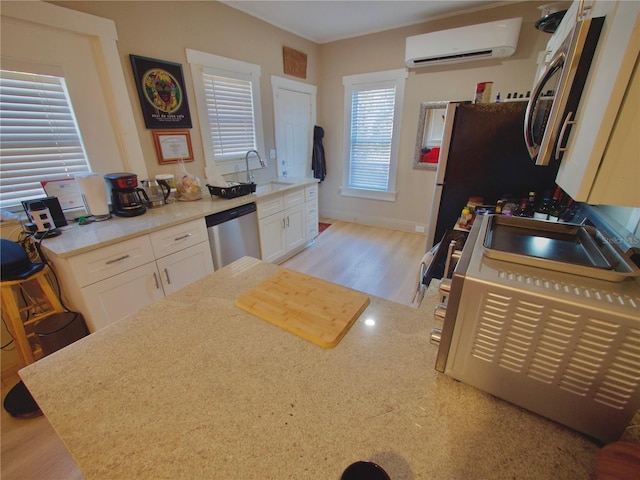 kitchen featuring white cabinetry, a wall mounted AC, sink, and stainless steel dishwasher