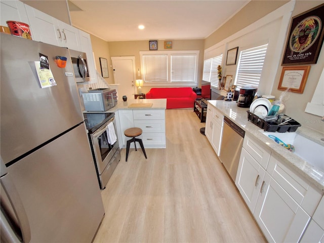 kitchen with white cabinetry, stainless steel appliances, light stone counters, and light wood-type flooring