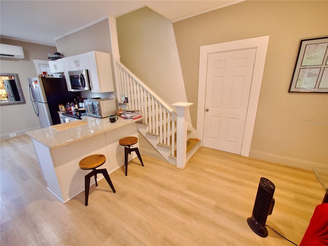 kitchen featuring light hardwood / wood-style flooring, appliances with stainless steel finishes, white cabinetry, a kitchen breakfast bar, and a wall mounted AC