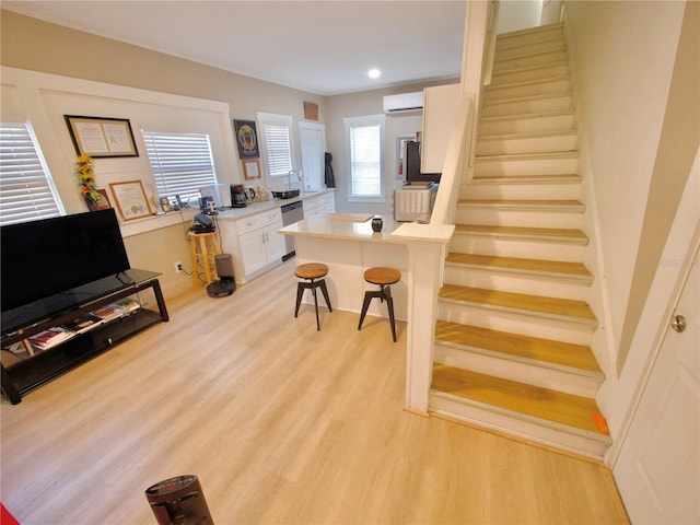 kitchen featuring an AC wall unit, a breakfast bar, dishwasher, white cabinets, and light wood-type flooring