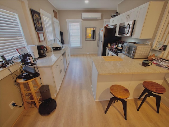 kitchen with a kitchen bar, white cabinetry, a wall mounted air conditioner, light wood-type flooring, and appliances with stainless steel finishes