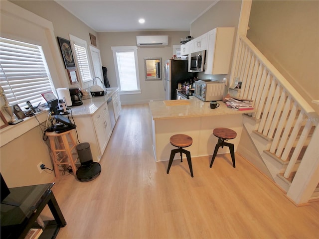 kitchen featuring appliances with stainless steel finishes, a wall mounted air conditioner, a kitchen breakfast bar, kitchen peninsula, and light wood-type flooring