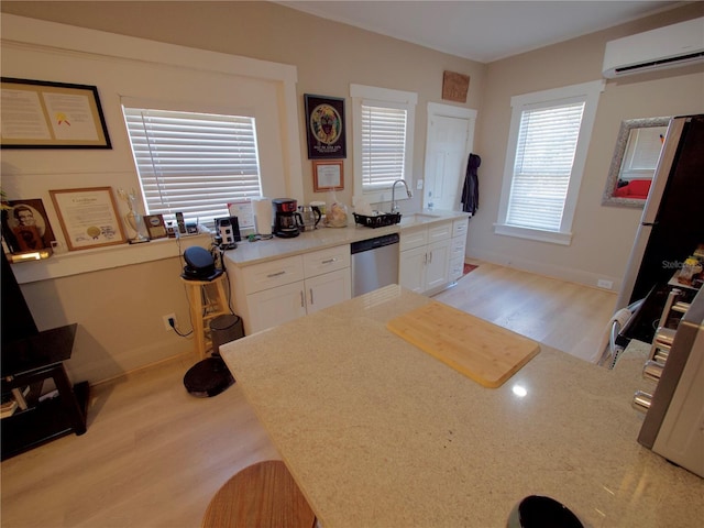 kitchen with a wall mounted air conditioner, sink, white cabinets, stainless steel dishwasher, and light hardwood / wood-style floors