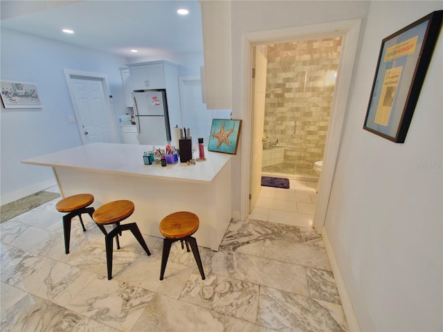 kitchen with white cabinetry, a breakfast bar, kitchen peninsula, and white fridge