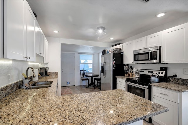 kitchen with sink, appliances with stainless steel finishes, white cabinetry, light stone counters, and kitchen peninsula