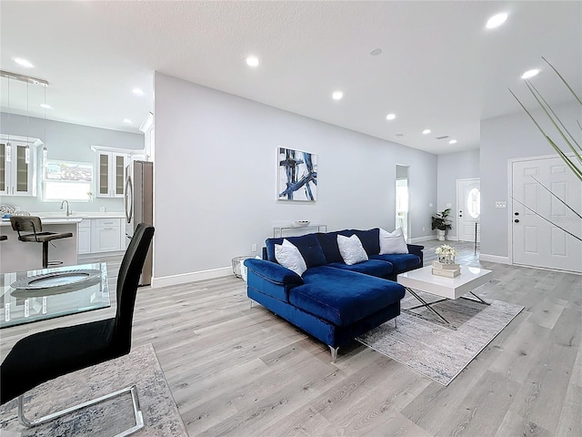 living room featuring lofted ceiling, sink, and light hardwood / wood-style floors