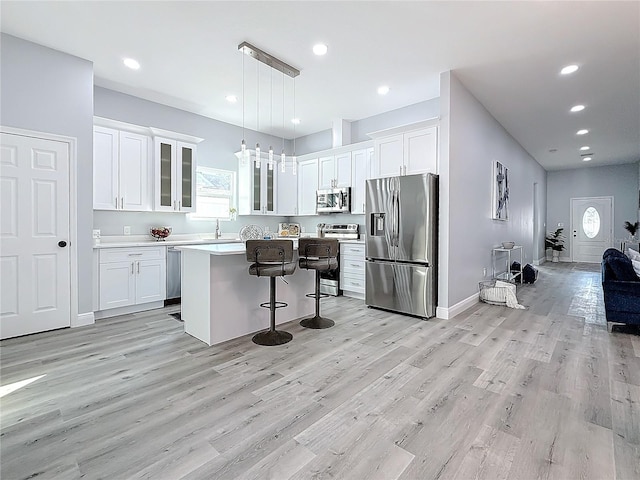 kitchen featuring appliances with stainless steel finishes, hanging light fixtures, a kitchen breakfast bar, a center island, and white cabinets