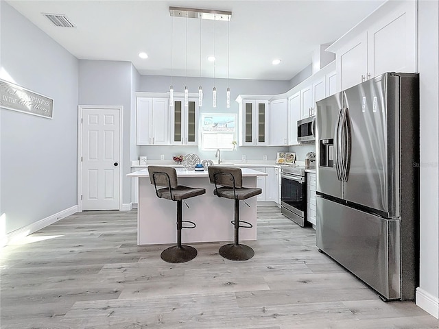 kitchen with a kitchen island, appliances with stainless steel finishes, decorative light fixtures, white cabinets, and a kitchen breakfast bar