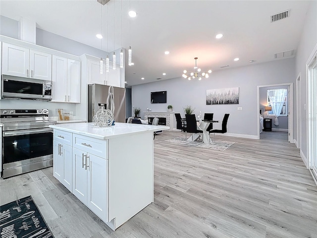 kitchen with stainless steel appliances, a center island, white cabinets, and decorative light fixtures